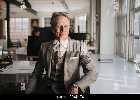 Lächelnder, reifer Geschäftsmann im Anzug, der am Schreibtisch sitzt Stockfoto