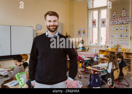 Porträt eines lächelnden bärtigen Lehrers, der vor Schülern im Klassenzimmer steht Stockfoto