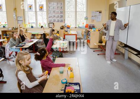 Lehrer steht am Whiteboard und stellt den Schülern im Klassenzimmer Fragen Stockfoto