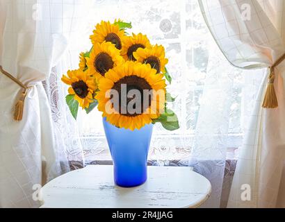 Ein Arrangement von hellen Sonnenblumen in einer blauen Vase. Stockfoto