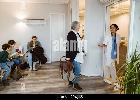 Seniorin-Patientin geht mit Arzt in der Klinik in den Untersuchungsraum Stockfoto