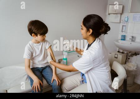 Seitenansicht einer Kinderärztin, die dem Jungen im Bett in der Klinik eine Impfung verabreicht Stockfoto