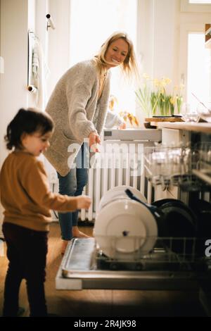 Glückliche Mutter und Sohn waschen Utensilien zu Hause in der Spülmaschine Stockfoto
