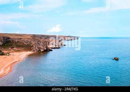 Meeresbucht mit Sandstrand und Hügeln. Touristen und Reisende ruhen sich am Ufer in einem Zeltlager aus. Stockfoto