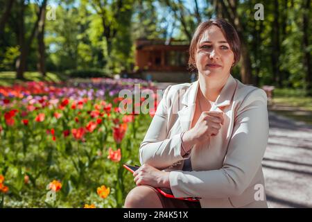 Porträt einer jungen Geschäftsfrau, die im Frühlingspark ein Tablet hält. Landschaftsdesignerin genießt die Ergebnisse blühender Tulpenbeete in der Kneipe Stockfoto