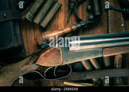 Antike 16-Gauge Break-Action glatt gebohrte Schrotflinte mit Messinggehäuse und Zubehör für Patronennachladung auf Holztisch. Stockfoto