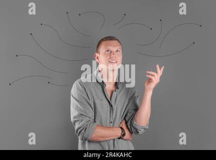 Berufswahl oder andere Lebensbereiche, Konzept. Entscheidungen treffen, aufmerksamer junger Mann, umgeben von gezeichneten Pfeilen auf farbigem Hintergrund Stockfoto