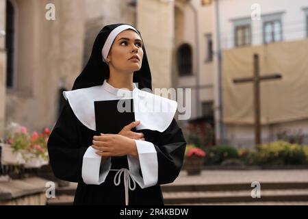 Junge Nonne mit Bibel in der Nähe von Gebäuden im Freien, Platz für Text Stockfoto