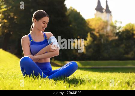 Glückliche Frau, die den Blutdruck mit einem modernen Monitor nach dem Training im Park kontrolliert. Platz für Text Stockfoto