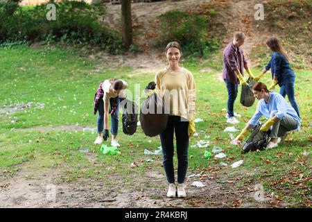 Junge Frau mit Plastiktüte und eine Gruppe von Leuten, die Müll im Park sammeln Stockfoto