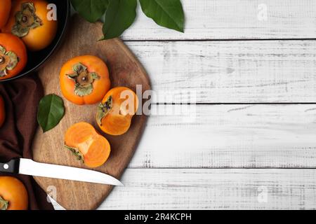 Ganze und geschnittene köstliche reife Persimonen auf weißem Holztisch, flach liegend. Platz für Text Stockfoto
