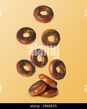 Viele frische Bagels mit Mohnsamen, die auf hellem orangefarbenen Hintergrund in den Stapel fallen Stockfoto