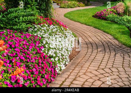 Blumenbeete von lebhaften, farbigen Ungeduldigen säumen einen gewundenen Gartenweg. Stockfoto