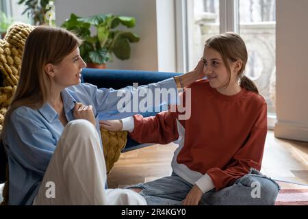 Junge, glückliche Mutter und Teenager-Tochter, die sich unterhalten, während sie auf dem Boden saßen Stockfoto