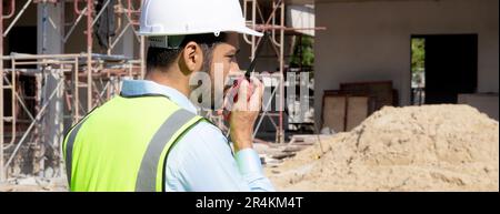 Ein junger Ingenieur, der Funkbefehle mit einem Arbeiter auf der Baustelle, einem Architekten oder einem Auftragnehmer verwendet, spricht mit dem Funkgerät, um die Entwicklung von Steuerungs- und Planungsfunktionen zu steuern Stockfoto