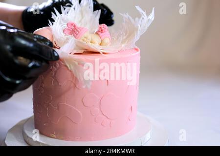 Dekoration eines Kuchens für eine Familie Taufe rosa Kuchen mit Fußabdrücken eines kleinen Kindes auf Engelsflügeln und Baby in rosa Windel ein Mädchen, wie man das Geschlecht des Kindes mithilfe eines Kuchens herausfinden kann Stockfoto