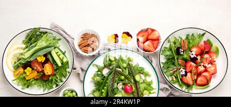 Köstliche Frühlingssalate mit essbaren Blumen, Gemüse, Obst, Mikrogreens und Käse auf weißem Hintergrund. Konzept der sauberen und gesunden Ernährung. Oben vi Stockfoto