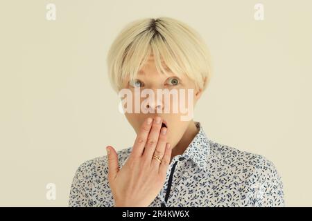 Blonde junge Frau bedeckt den Mund mit Handfläche in Erstaunen Stockfoto
