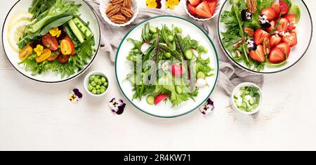 Köstliche Frühlingssalate mit essbaren Blumen, Gemüse, Obst, Mikrogreens und Käse auf weißem Hintergrund. Konzept der sauberen und gesunden Ernährung. Oben vi Stockfoto