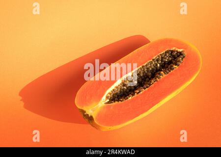 Reife Papaya-Früchte, halbiert auf orangefarbenem Hintergrund. Sommerzeitkonzept. Stockfoto