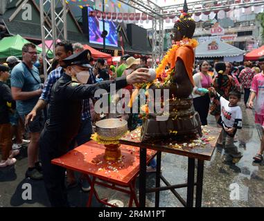 Ein thailändischer Polizist streut sauberes und duftendes Wasser über eine Buddha-Statue, um sie zu reinigen und ihr Glück während des Songkran Festivals zu sichern. Bangkok, Thailand Stockfoto