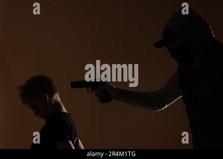 Der Kidnapper zielt mit der Waffe auf einen kleinen Jungen, der auf dunklem Hintergrund als Geisel genommen wurde Stockfoto