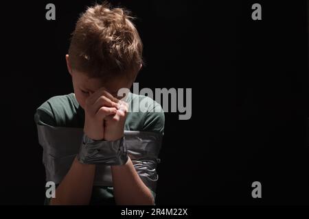 Ein kleiner Junge gefesselt und auf dunklem Hintergrund als Geisel genommen. Platz für Text Stockfoto