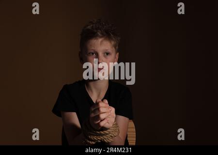 Ein kleiner Junge gefesselt und auf dunklem Hintergrund als Geisel genommen Stockfoto