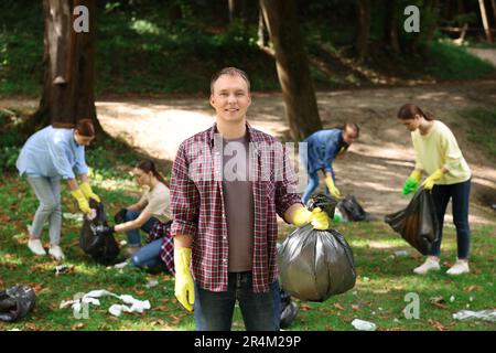 Junger Mann mit Plastiktüte und eine Gruppe von Leuten, die Müll im Park sammeln Stockfoto