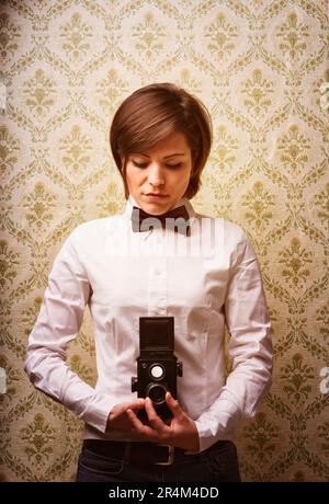 Der Fotograf fokussiert eine Reflexkamera mit zwei Objektiven und schaut in den hüfthohen Sucher. Tapetenhintergrund aus den 70s Jahren, altmodische Fotofarbe. Traditio Stockfoto