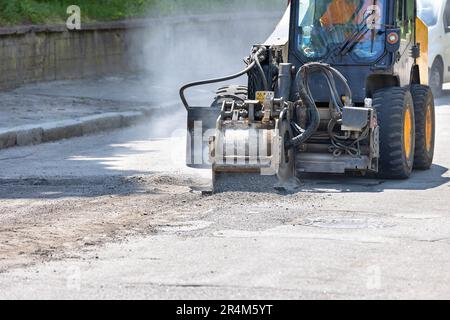 Ein Straßentraktor für Bauarbeiten mit einer leistungsstarken Fräsvorrichtung entfernt eine Schicht alten Asphalts auf der Fahrbahn. Stockfoto