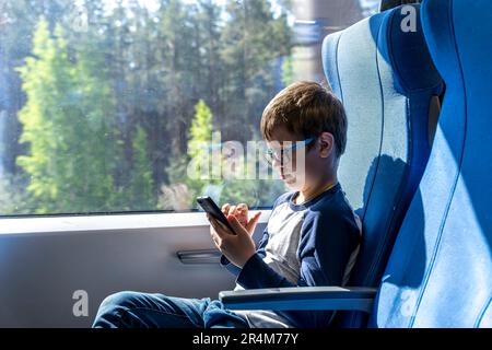 Ein süßer weißer Schuljunge mit Brille fährt einen Pendlerzug Stockfoto