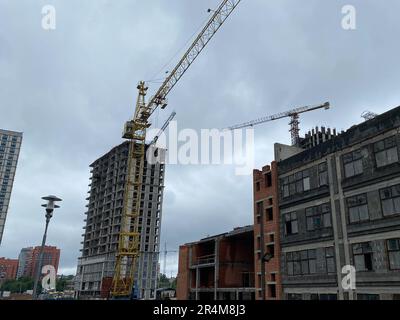 Neubau von Häusern mit Kränen und Baumaschinen im Mikrobezirk einer Grossstadt. Stockfoto