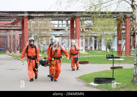 Vier professionelle Feuerwehrleute in orangefarbenen feuerfesten Schutzanzügen, weißen Helmen und Gasmasken tragen die verletzte Person auf Tragen von Stockfoto