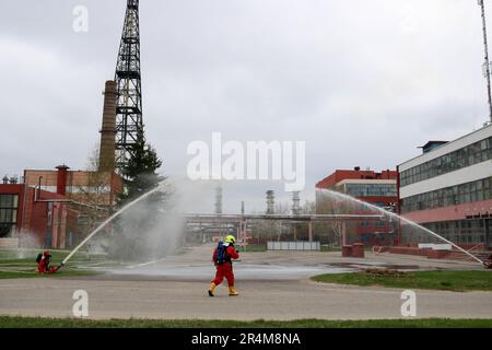 Professionelle Feuerwehrleute in orangefarbenen feuerfesten Anzügen in weißen Helmen mit Gasmasken testen Feuerlöschschläuche und Feuerwaffen, um einen Brand zu löschen Stockfoto