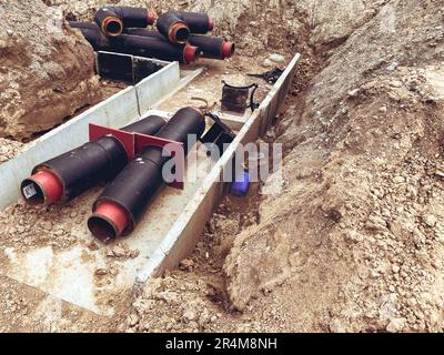 Bau einer neuen Nachbarschaft. Ich verlegte Kommunikationen, Rohre auf dem Boden. Breites, schwarzes Rohr mit rotem Boden für die Kanalisation. Stockfoto