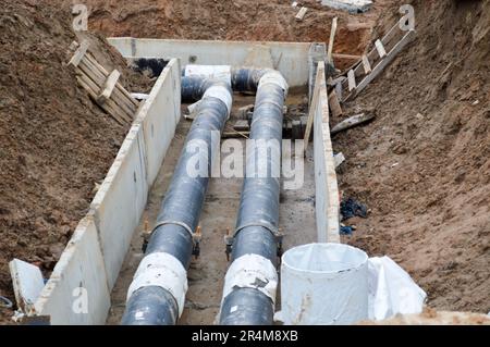 Große schwarze Metall- und Plastikwasserrohre für heißes und kaltes Wasser auf einer Baustelle während einer Reparatur in einer neuen Nachbarschaft unter dem Boden. Stockfoto