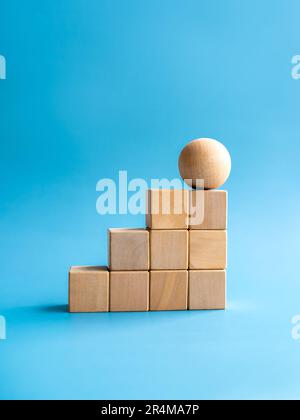 Holzkugel auf Holzwürfel Blockdiagramm Schritte auf blauem Hintergrund, vertikaler Stil. Geschäftswachstumsprozess, Trend, Entwicklung, Veränderung, Stockfoto