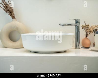 Sauberes, minimalistisches Badezimmer oder Badezimmer mit modernem rundem Waschbecken, Wasserhahn, grünen Blättern in modernen Töpfen auf Marmorboden und weißem Boden Stockfoto