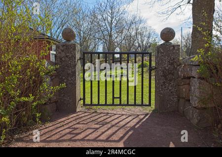 Eingang eines Friedhofs mit altem schmiedeeisernem Tor auf Steinpfählen. Stockfoto