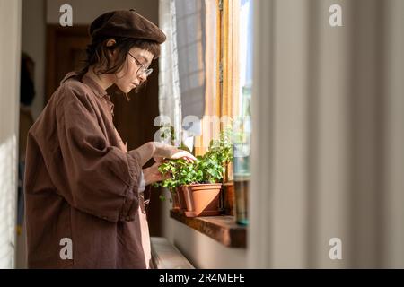 Hipstermädchen kümmert sich um Zimmerpflanzen, prüft, ob die Pflanze gesund ist. Pflanzenliebhaber. Stockfoto