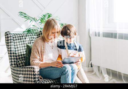 Ältere Frau und Sohn Kind spielen mit Tablet-pc. Lächelnde Frau und ihr Enkel sitzen zu Hause mit Gadget digitalen Gerät für Online-Shopping Internet Stockfoto