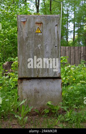 Die alte, graue, geschlossene Schachtel für Elektrizität steht in einem grünen Gras Stockfoto