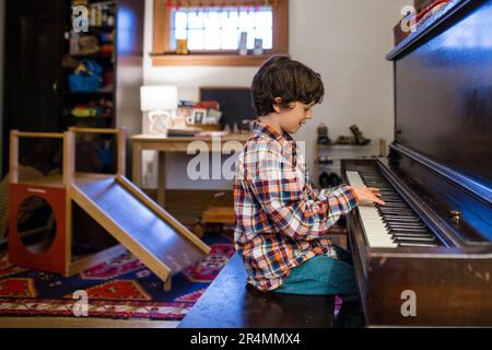 Seitenansicht eines Kindes, das im Fensterlicht sitzt und Klavier praktiziert Stockfoto