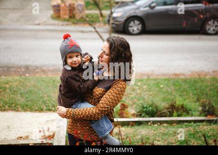 Eine mutter steht zärtlich in ihrem Garten und hält ein lächelndes Kind in den Armen Stockfoto