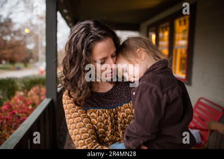 Eine Mutter hält ihr Kind auf der Veranda und legt seinen Kopf sanft auf seine Stockfoto