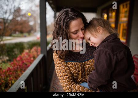 Eine lächelnde Mutter und ein lächelndes Kind kuscheln am Abend auf der Veranda Stockfoto