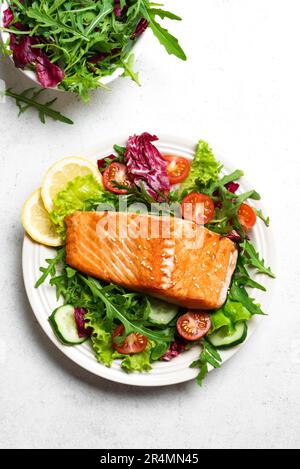 Gegrilltes Lachsfilet und frischer Gemüsesalat mit Tomaten, Salat und Rucola. Gesundes Keto Food - grüner Salat und gerösteter Lachs auf weißem Backgr Stockfoto