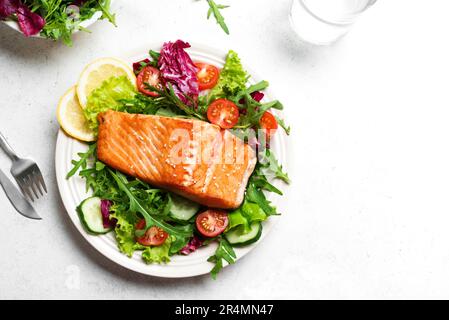 Gegrilltes Lachsfilet und frischer Gemüsesalat mit Tomaten, Salat und Rucola. Gesundes Keto Food - grüner Salat und gerösteter Lachs auf weißem Backgr Stockfoto