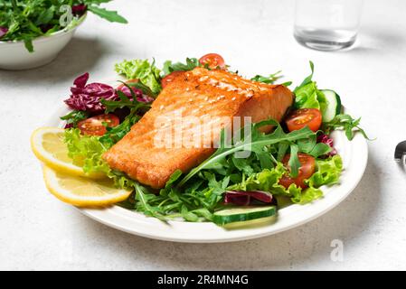 Gegrilltes Lachsfilet und frischer Gemüsesalat mit Tomaten, Salat und Rucola. Gesundes Keto Food - grüner Salat und gerösteter Lachs aus der Nähe. Stockfoto